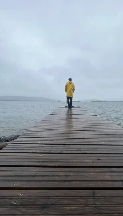 person im gelben regenmantel auf dem steg am see